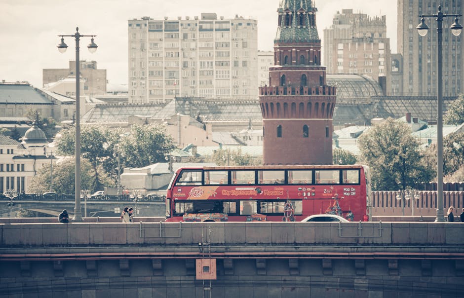 A red double-decker bus in front of Moscow's iconic architecture on a sunny day.