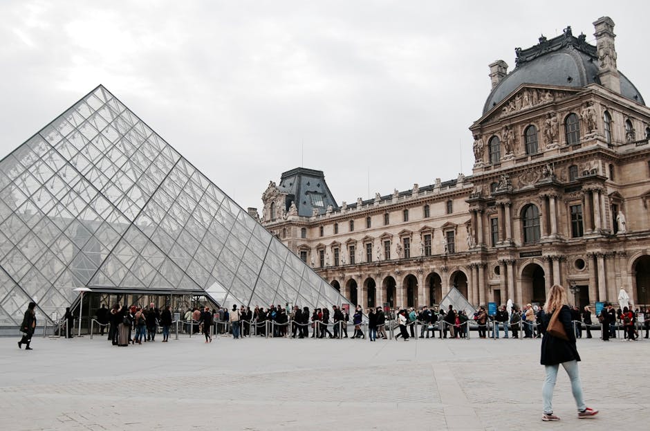 Visitors gather at the glass pyramid entrance of the Louvre Museum in Paris, capturing the blend of modern and classic architecture.