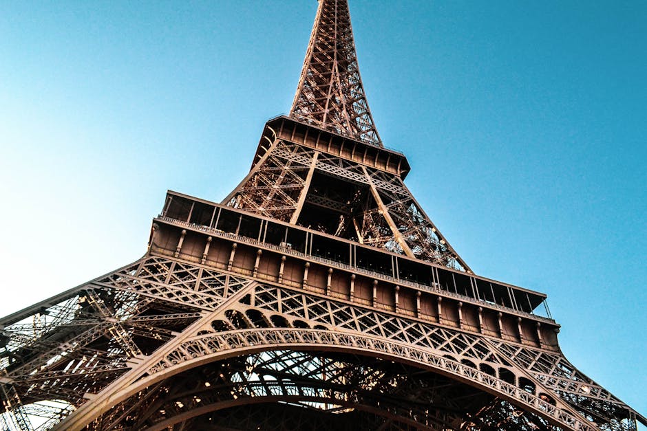 An iconic view of the Eiffel Tower from a low angle, highlighting its intricate iron lattice structure against a clear blue sky.